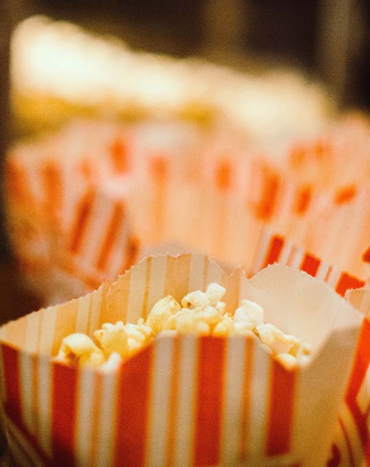 Red and white bags of popcorn are lined up in a darkened room in front of the popcorn making machine.